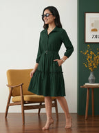 Woman in a green dress standing in a room with a yellow chair and a vase of flowers.