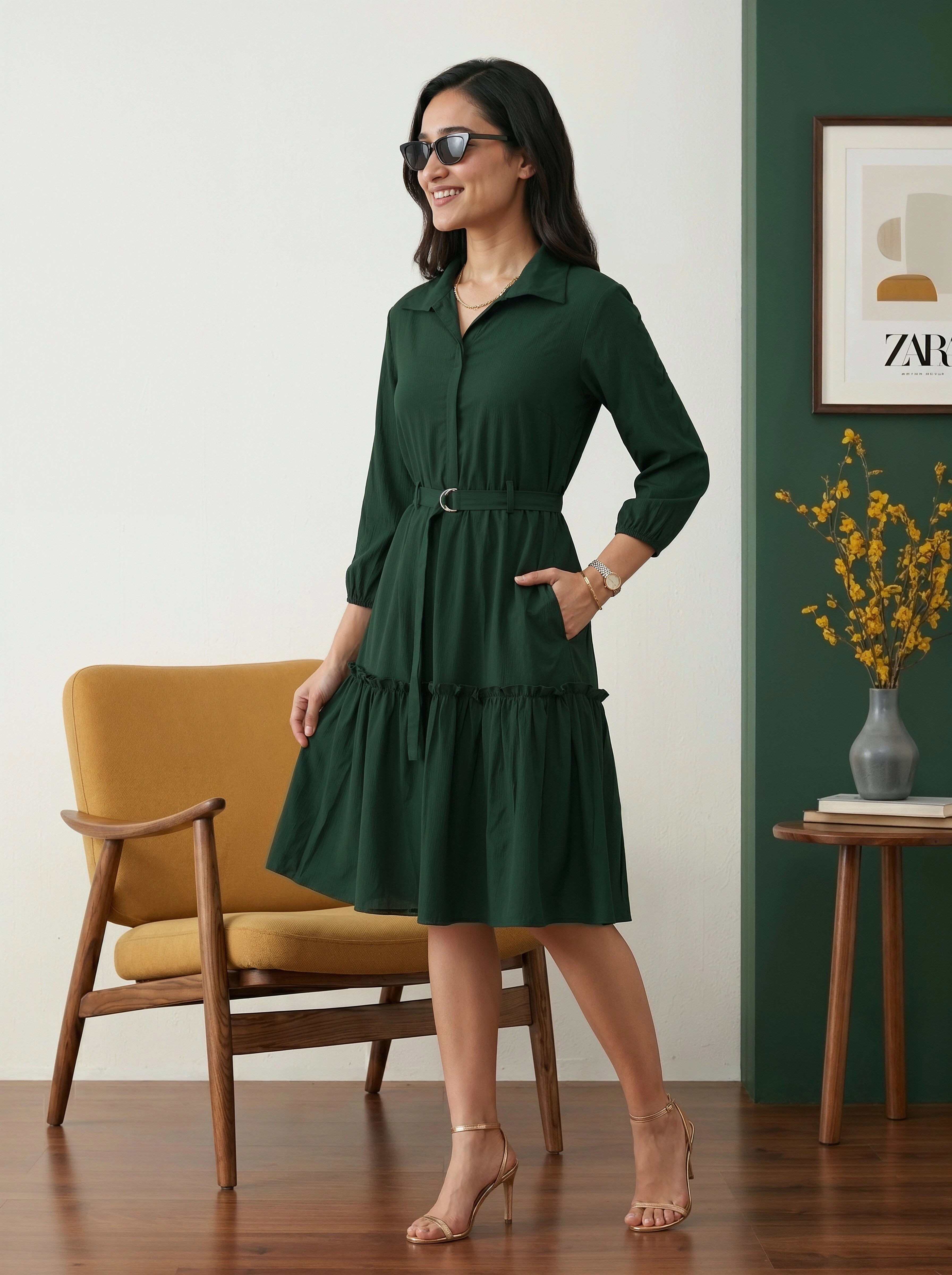 Woman in a green dress standing in a room with a yellow chair and a vase of flowers.