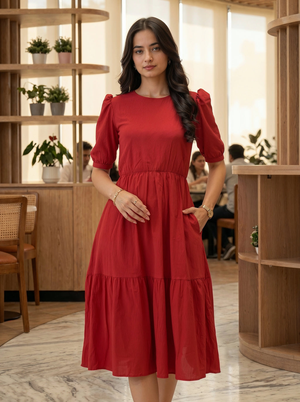 Woman standing in a modern, sunlit cafe wearing a sophisticated red tiered midi dress with puff sleeves.