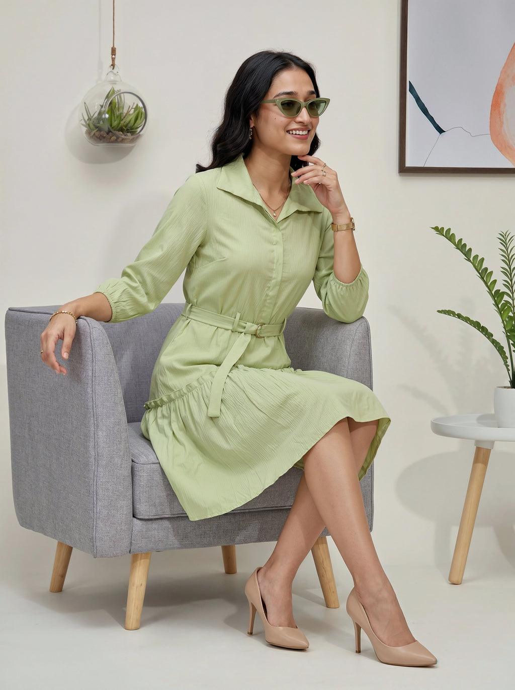Woman in a light green dress sitting on a gray chair in a modern interior setting.