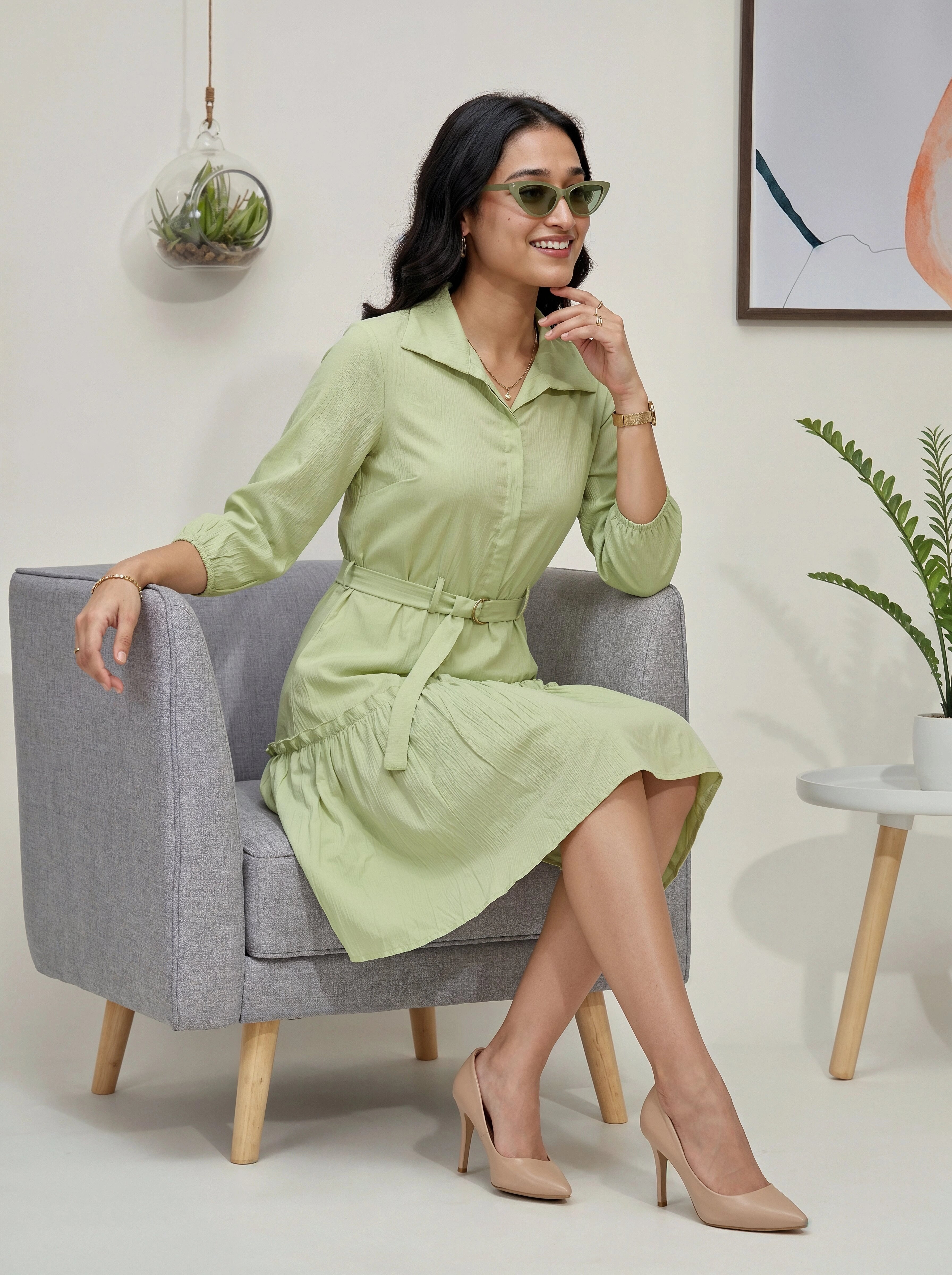 Woman in a light green dress sitting on a gray chair in a modern interior setting.