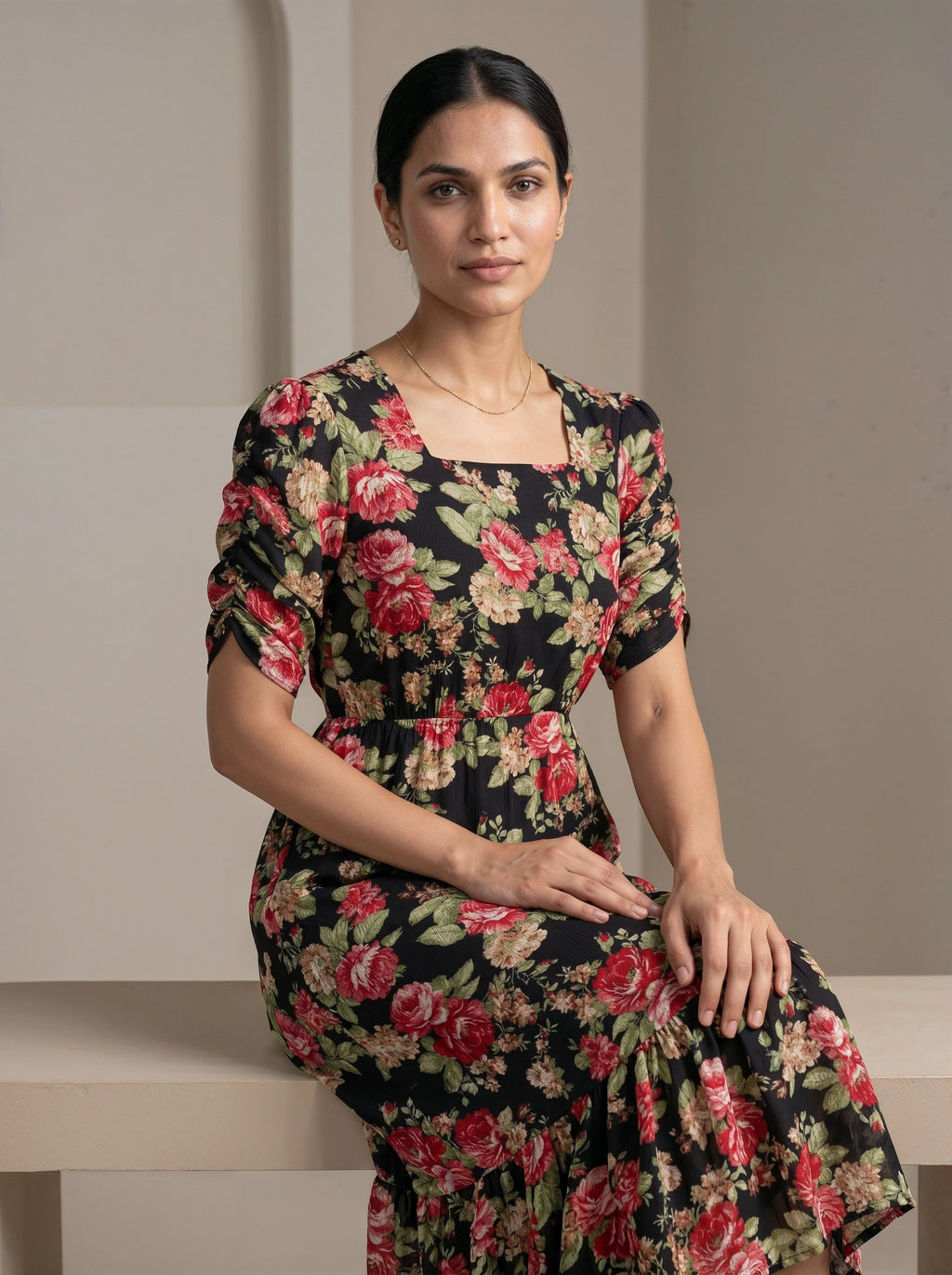 Woman wearing a floral dress sitting on a bench against a plain background