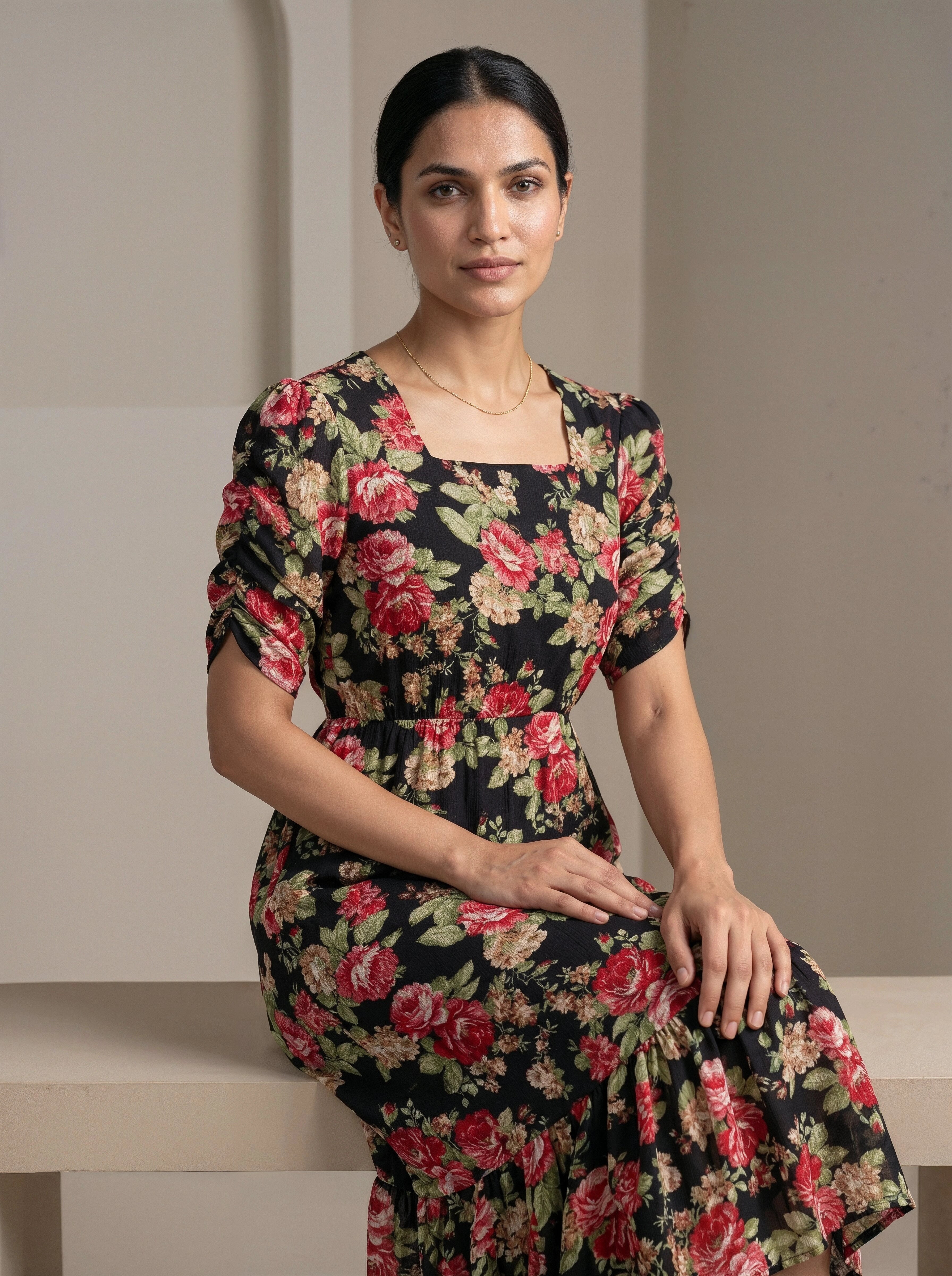 Woman wearing a floral dress sitting on a bench against a plain background
