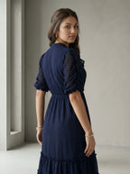Woman wearing a blue dress standing against a white wall.