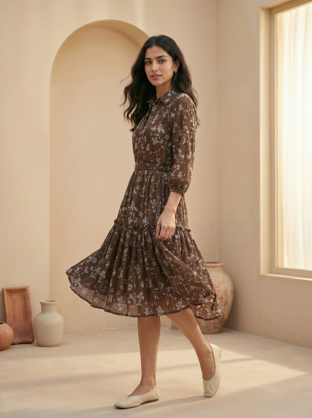 Woman wearing a brown floral dress in a warm-toned room with arched door and window.