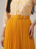 Person wearing a yellow floral shirt and mustard yellow pleated skirt against a neutral background