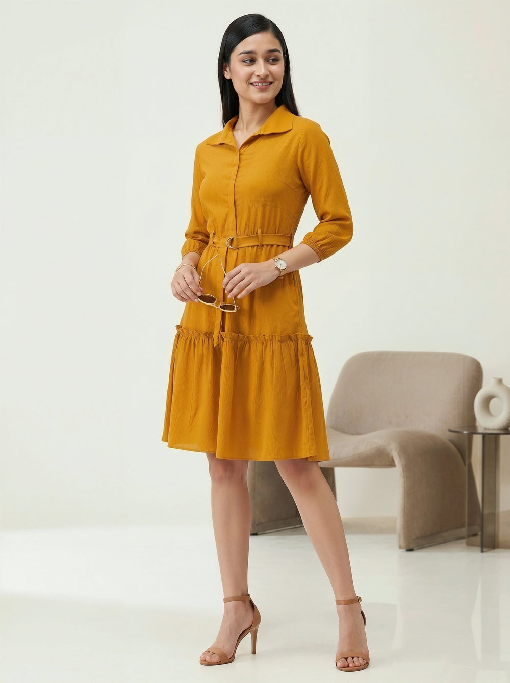 Woman wearing a mustard yellow dress standing in a minimalistic room.