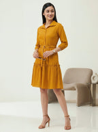 Woman wearing a mustard yellow dress standing in a minimalistic room.