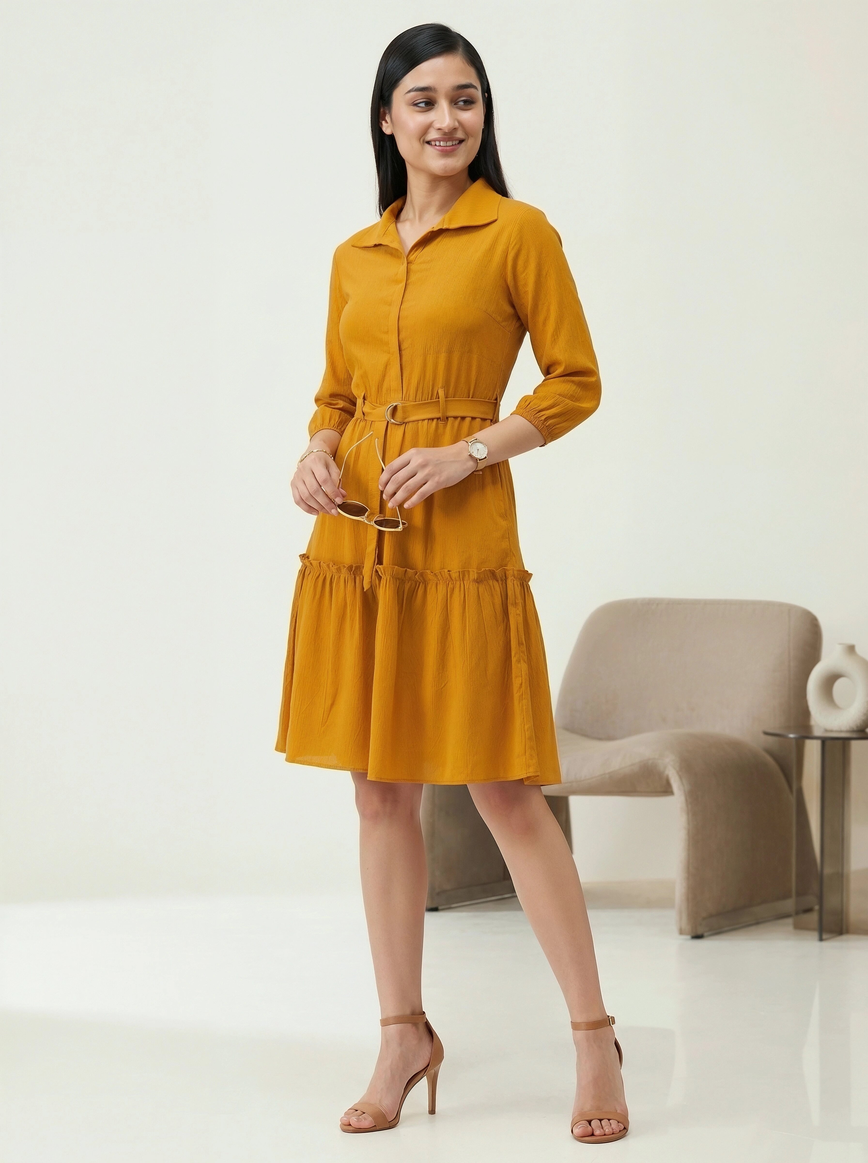 Woman wearing a mustard yellow dress standing in a minimalistic room.