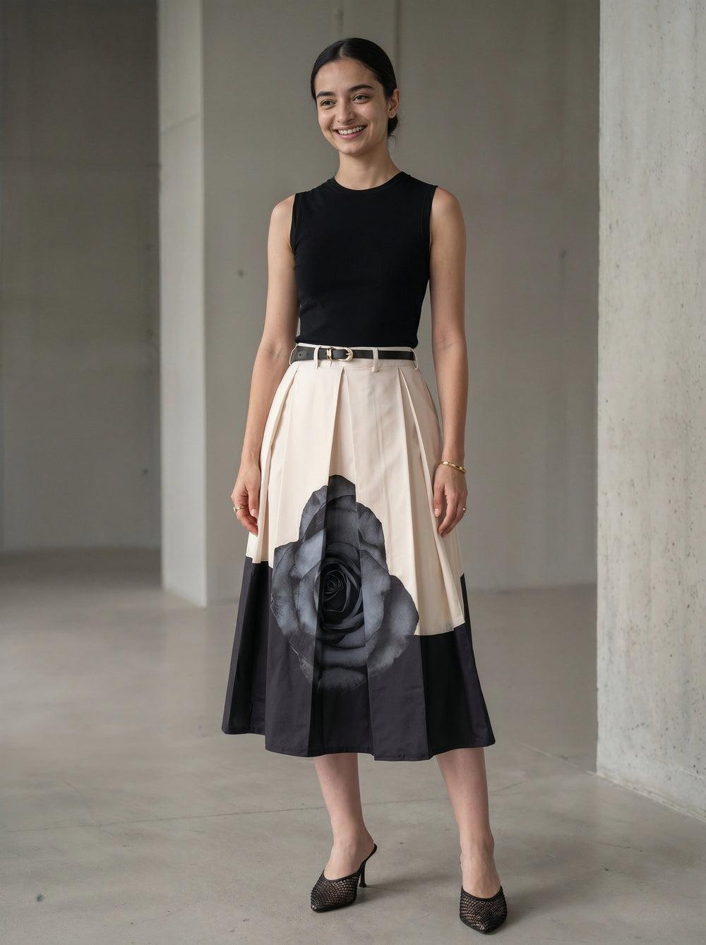 Woman wearing a black sleeveless top and a beige skirt with a large black floral design, standing in a minimalistic room.