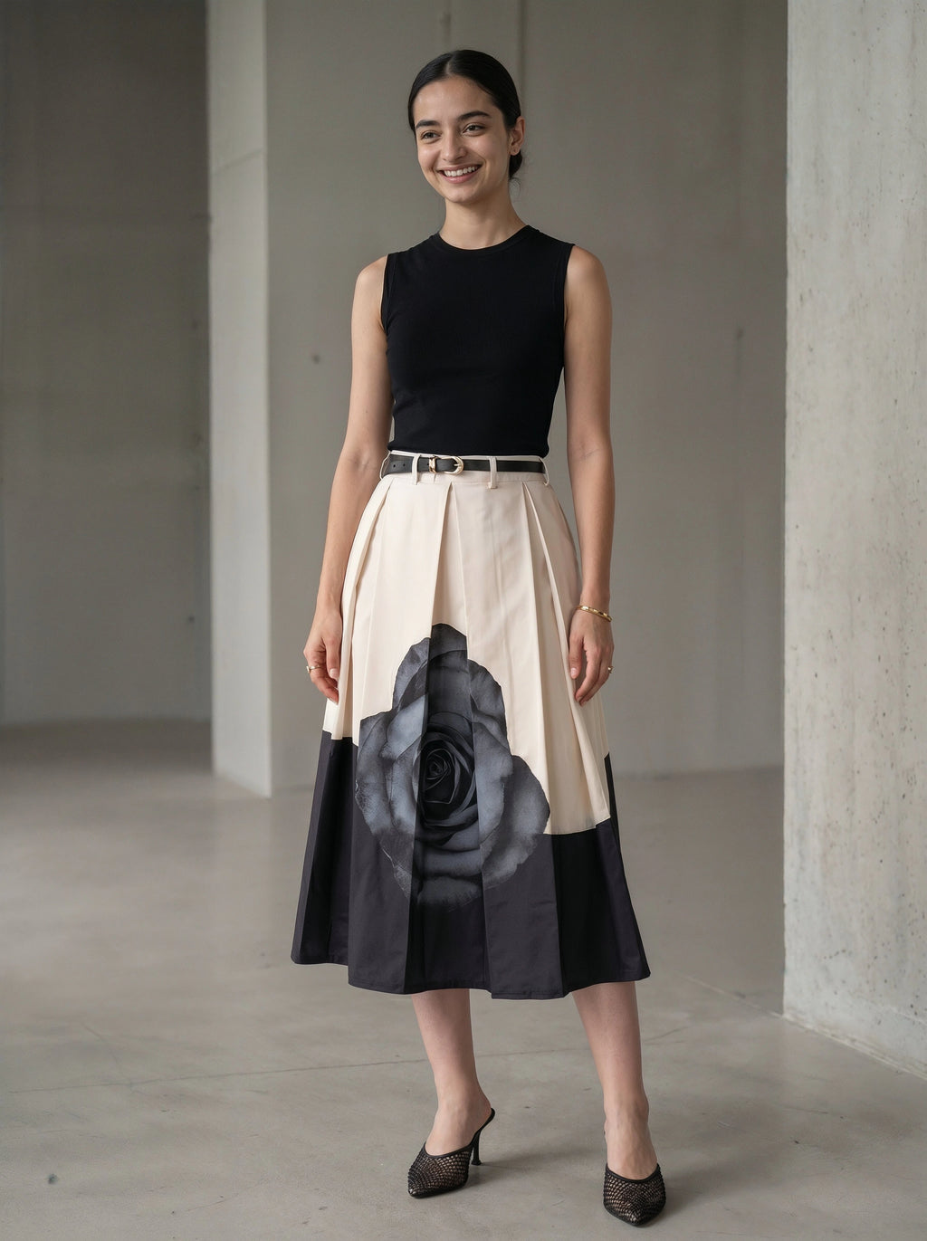 Woman wearing a black sleeveless top and a beige skirt with a large black floral design, standing in a minimalistic room.