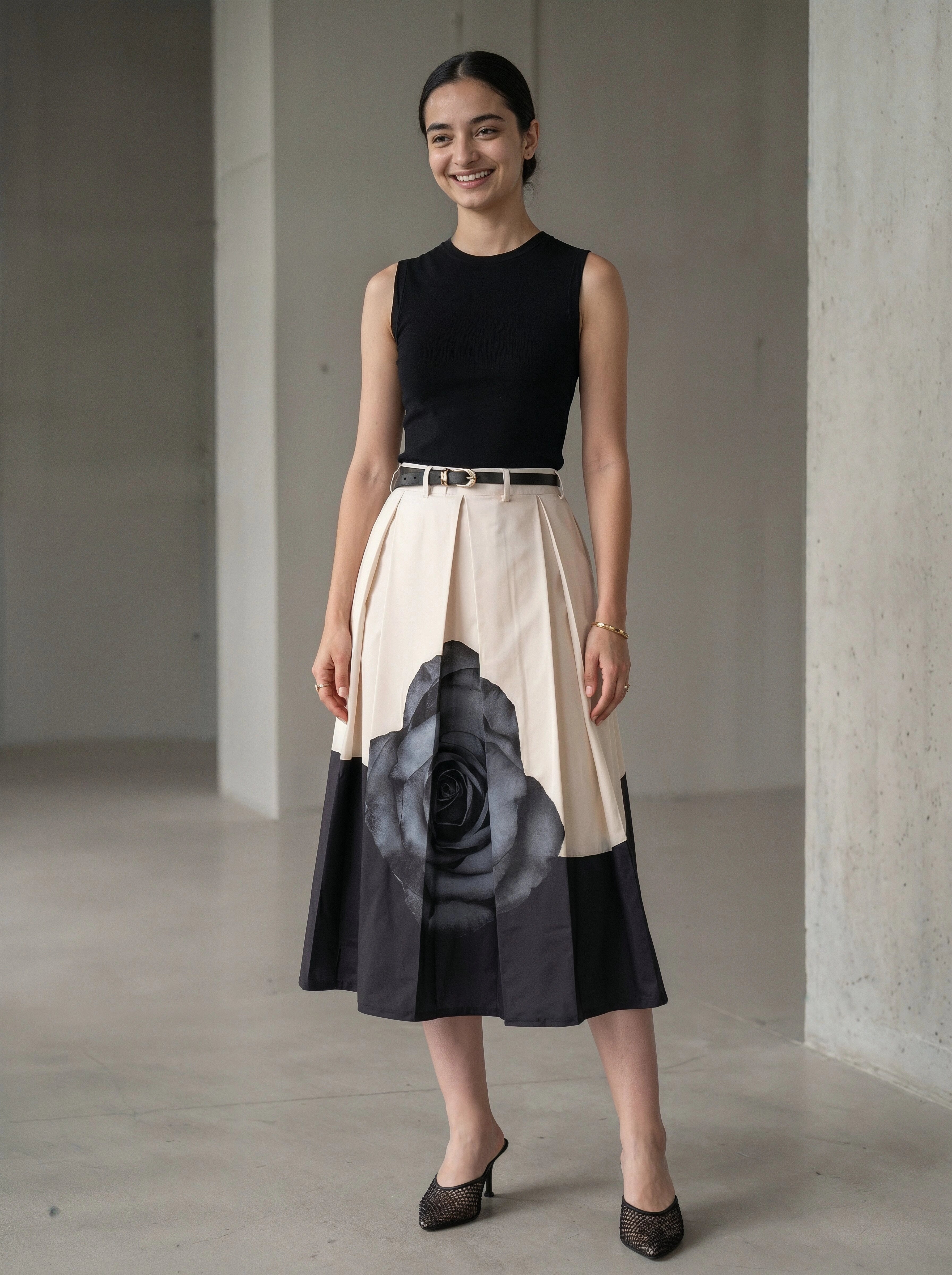 Woman wearing a black sleeveless top and a beige skirt with a large black floral design, standing in a minimalistic room.