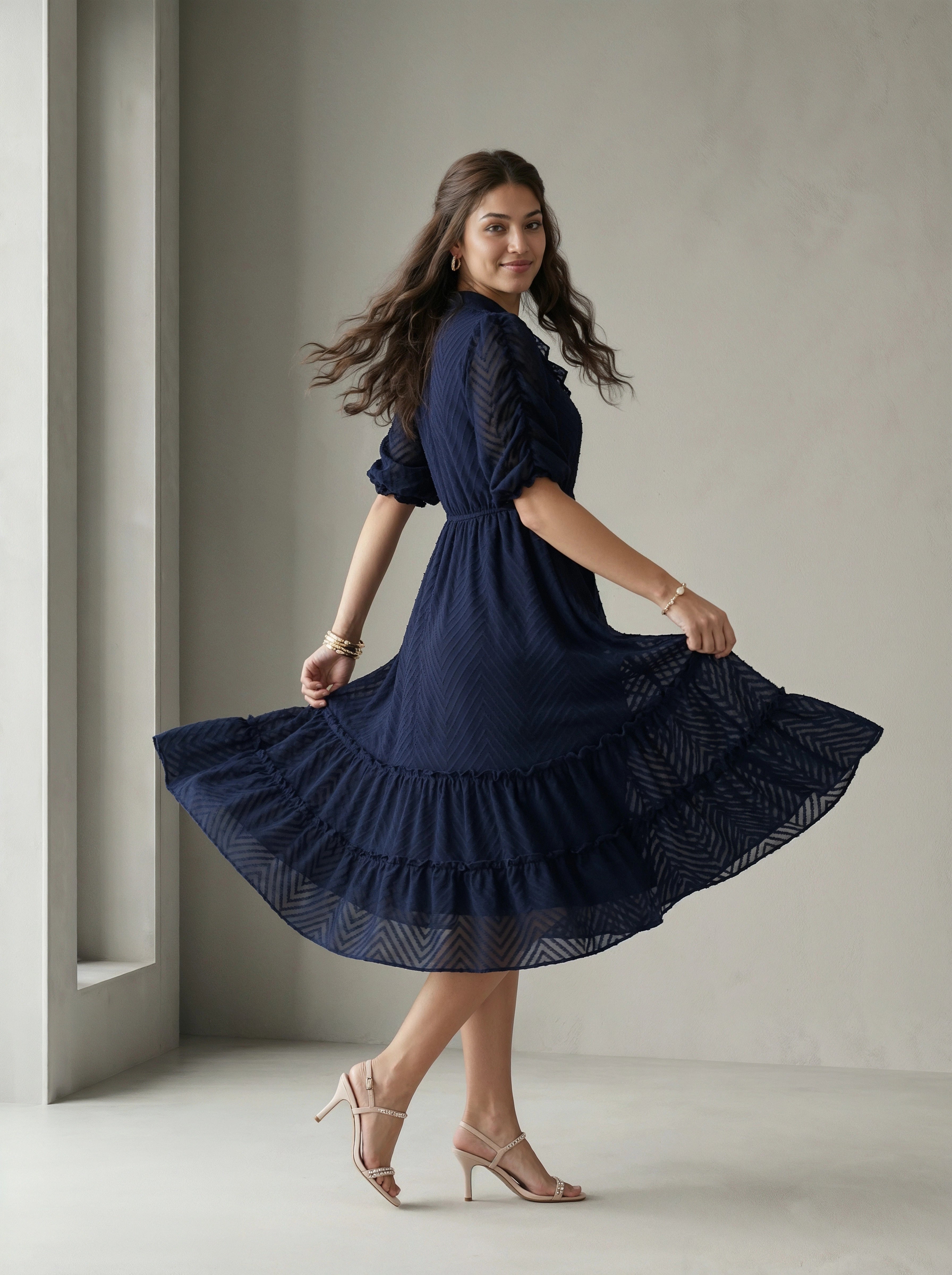 Woman wearing a blue dress standing in front of a white wall with a window.
