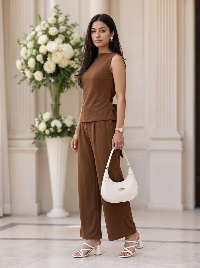 A woman modeling a brown tiered midi dress with short puff sleeves and side pockets, standing in a bright room with a wooden floor and a potted plant.