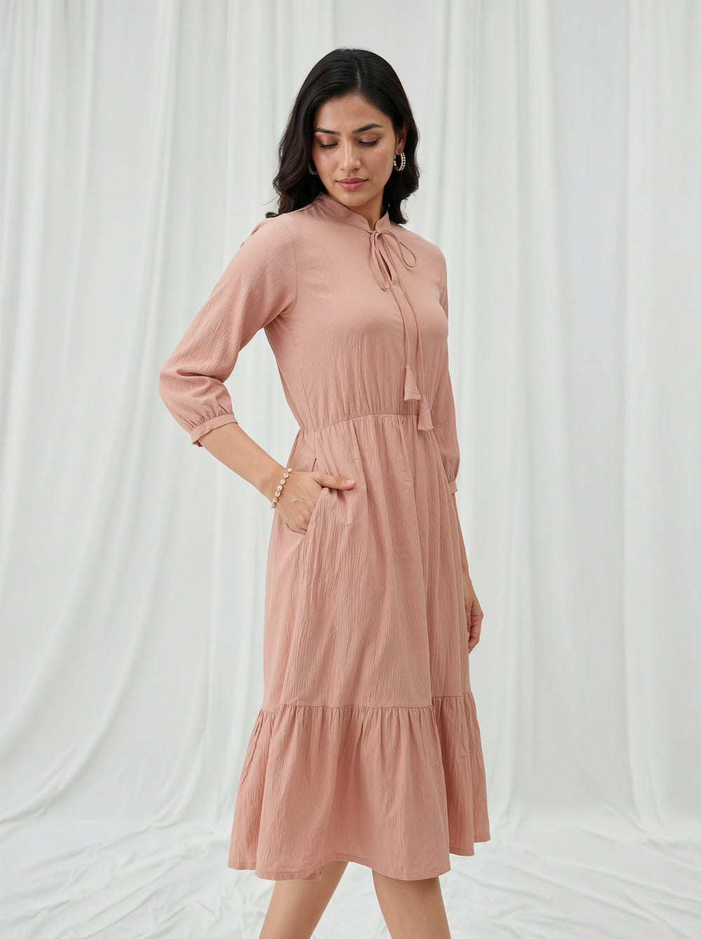 Woman wearing a cream dress against a white curtain background