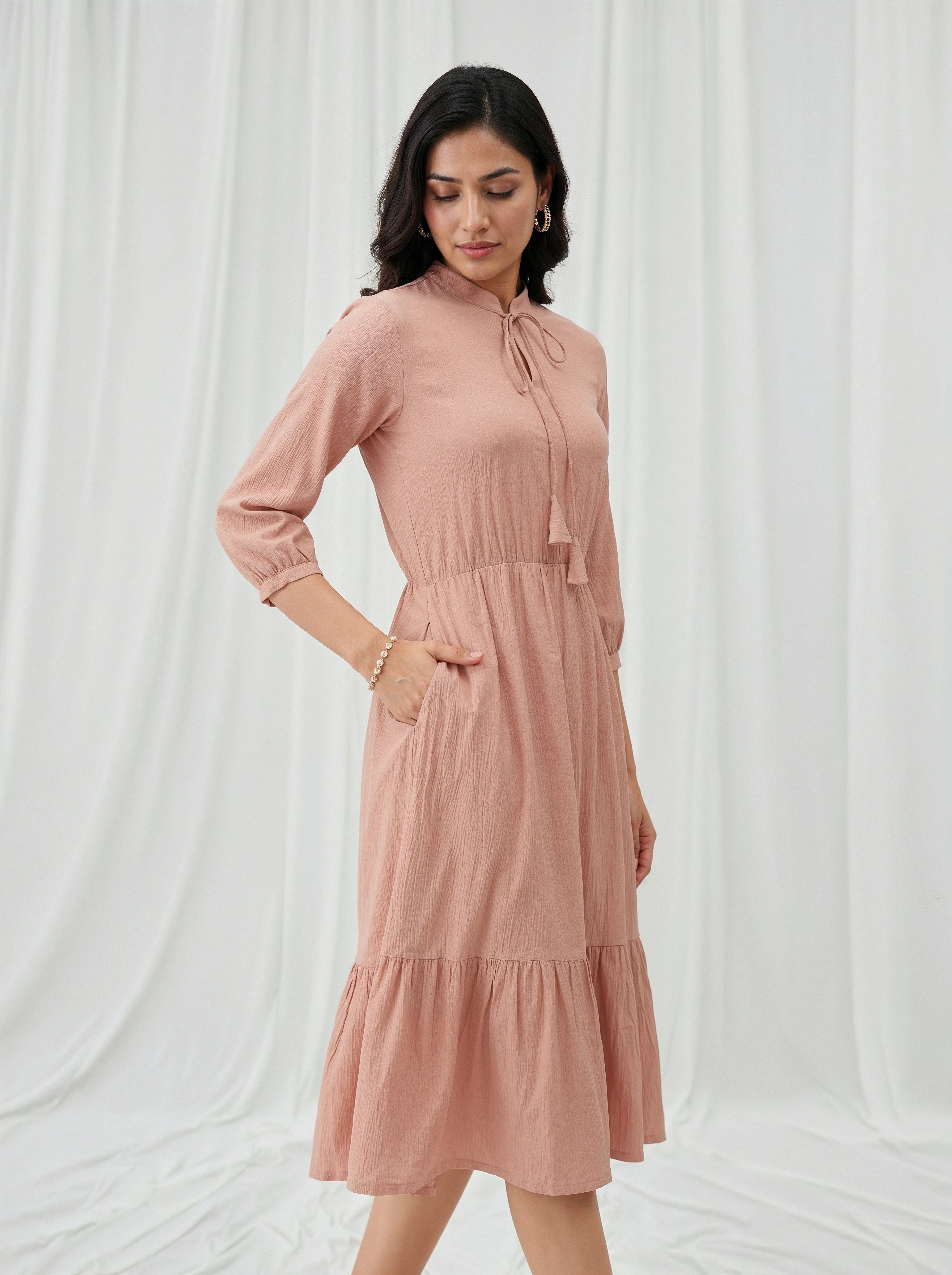 Woman wearing a cream dress against a white curtain background