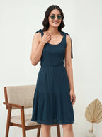 Woman wearing a dark blue dress with ruffled shoulders in a minimalistic setting.
