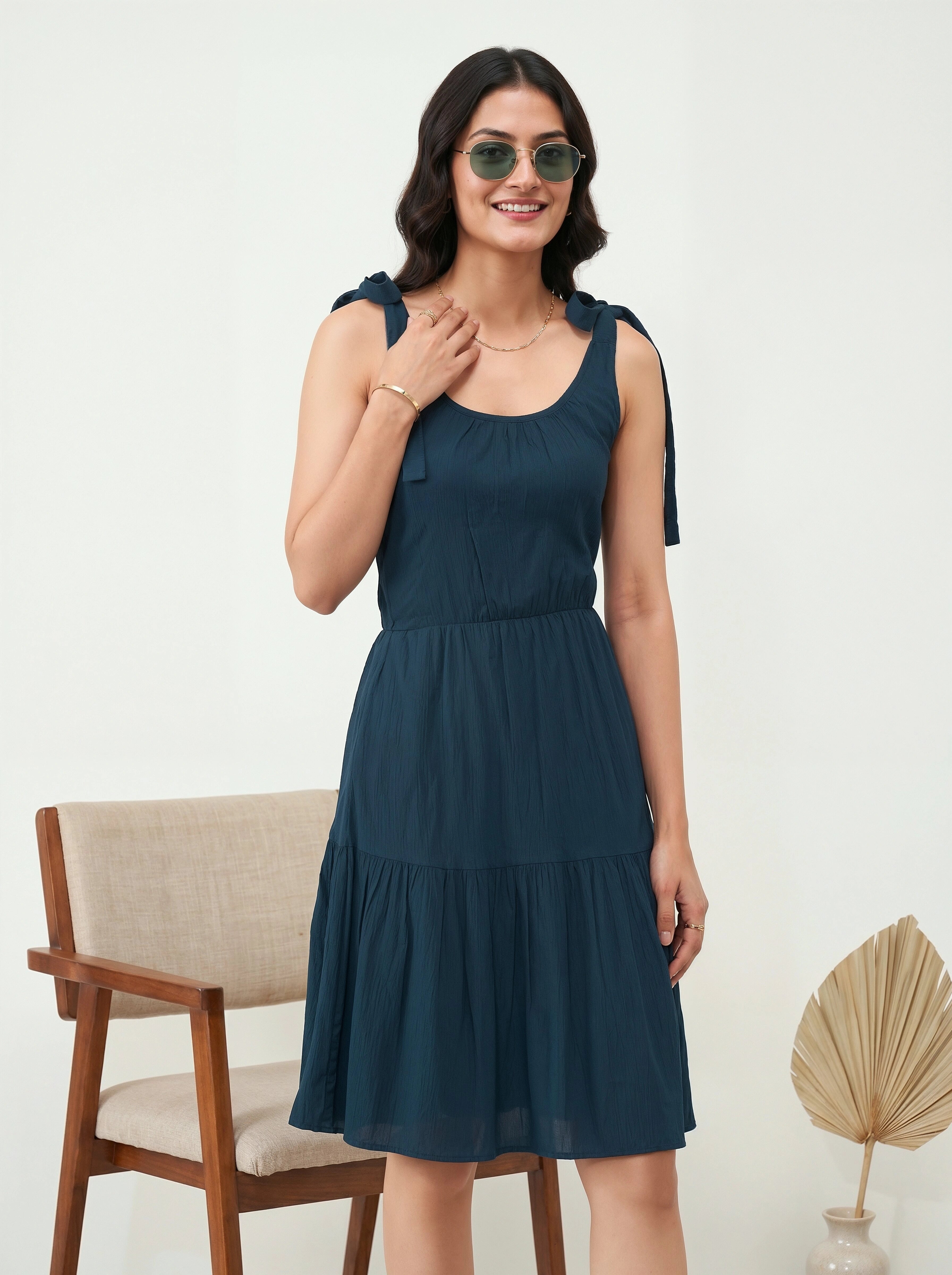 Woman wearing a dark blue dress with ruffled shoulders in a minimalistic setting.