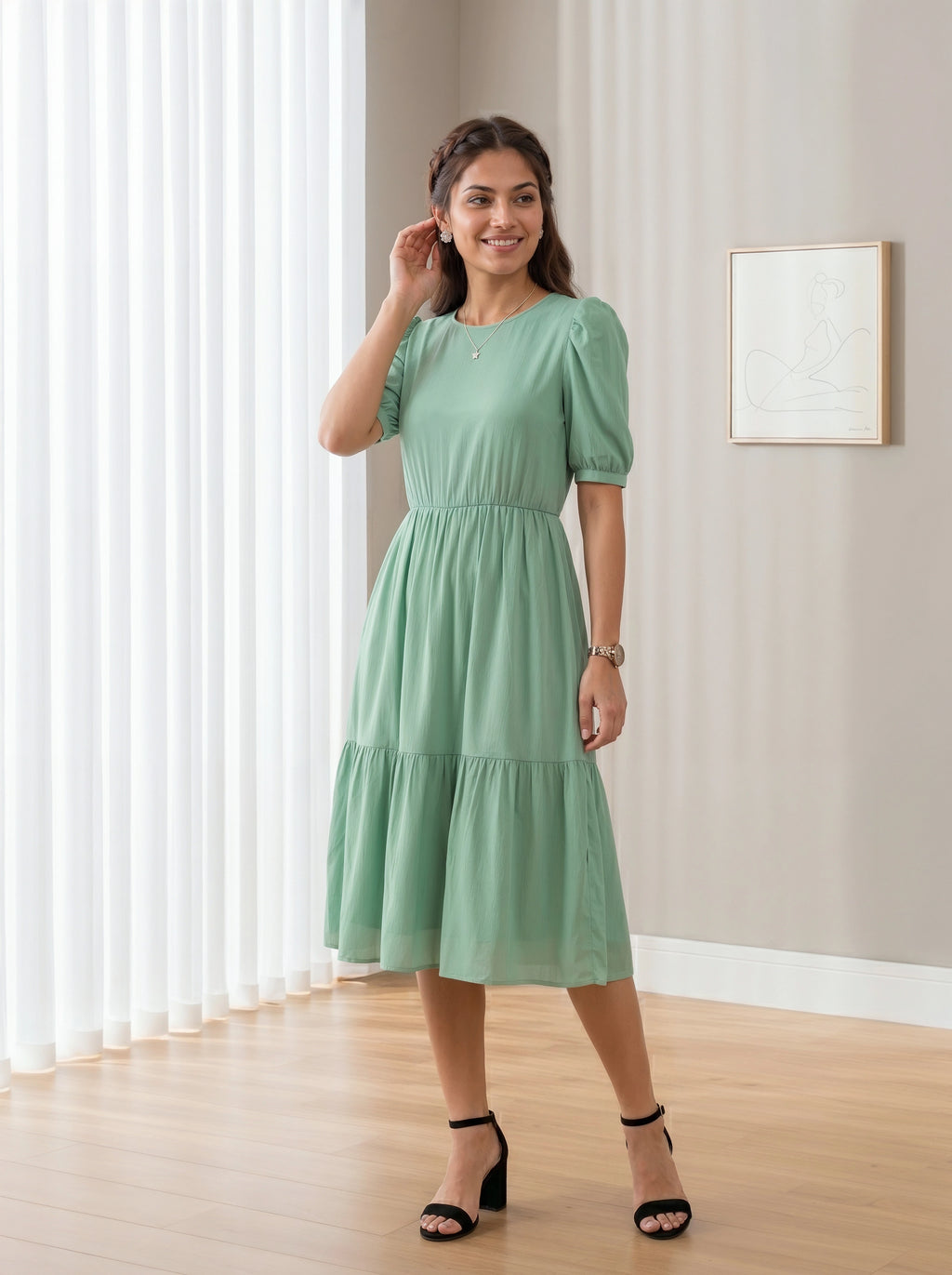 Woman wearing a green dress standing in a room with light-colored walls and wooden floor.