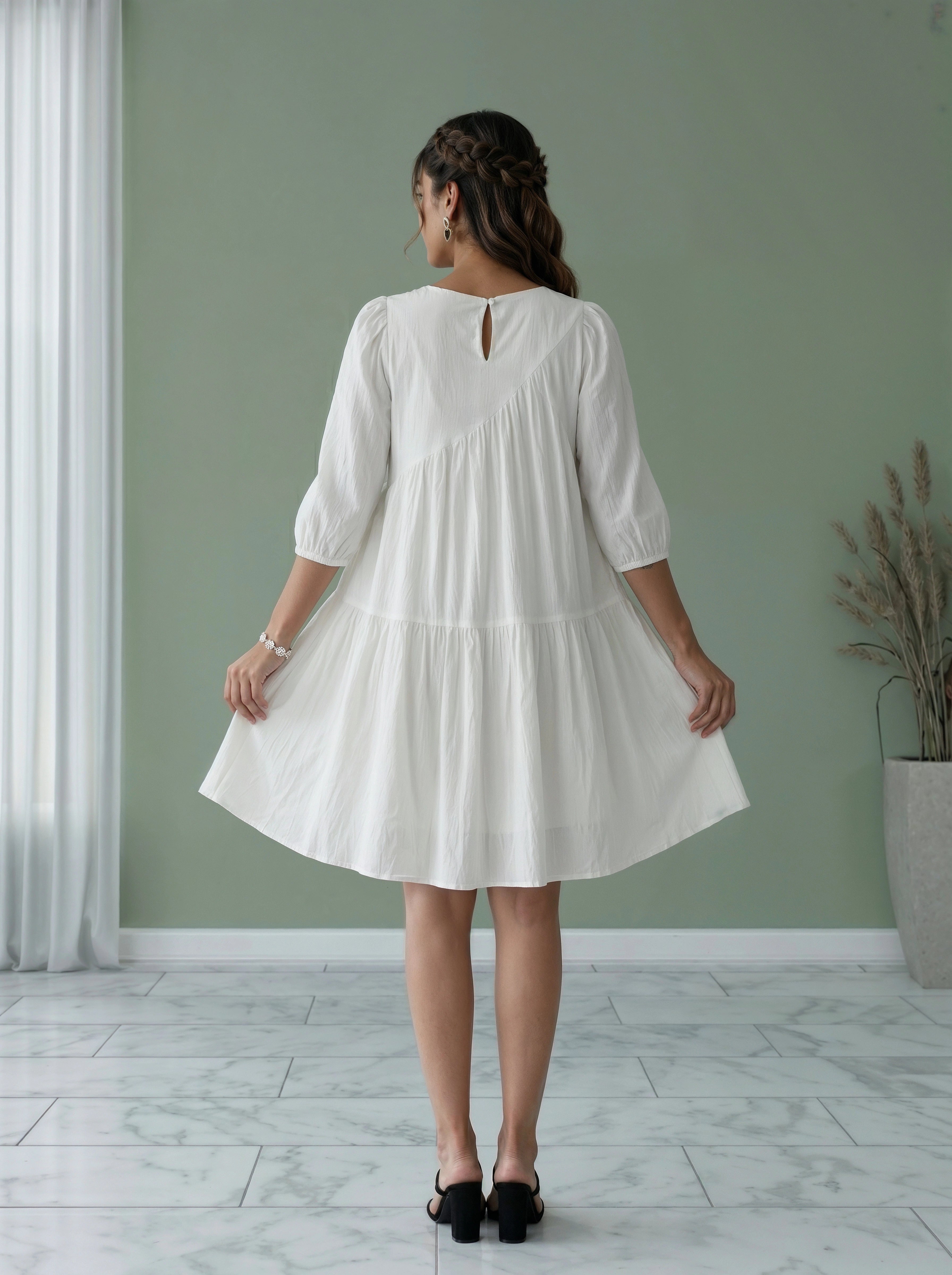 Woman wearing a white dress standing in a room with a green wall and a plant.