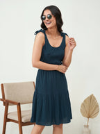 Woman wearing a navy blue dress with bow straps, standing against a white background.