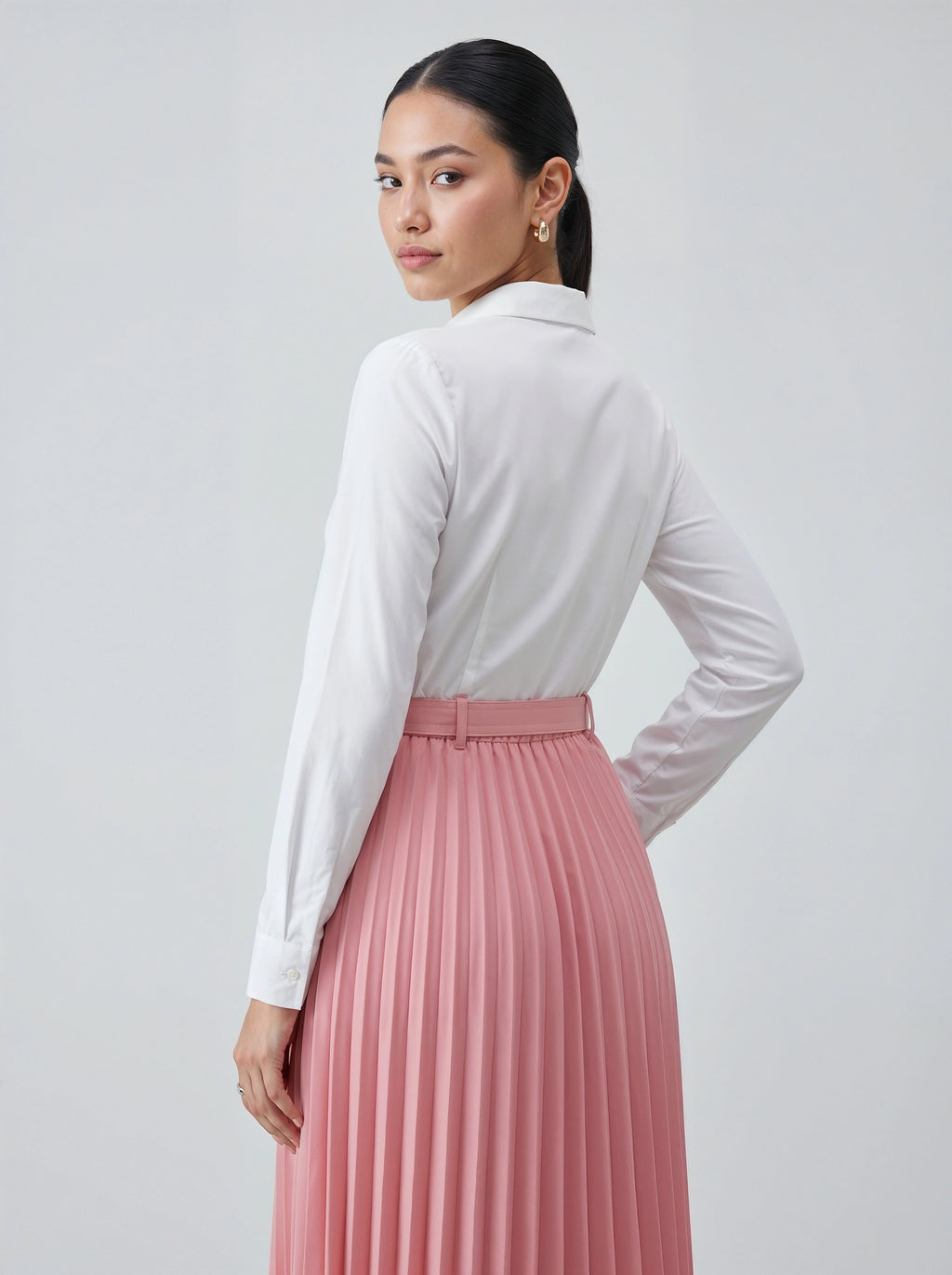 Woman wearing a white blouse and pink pleated skirt on a plain background