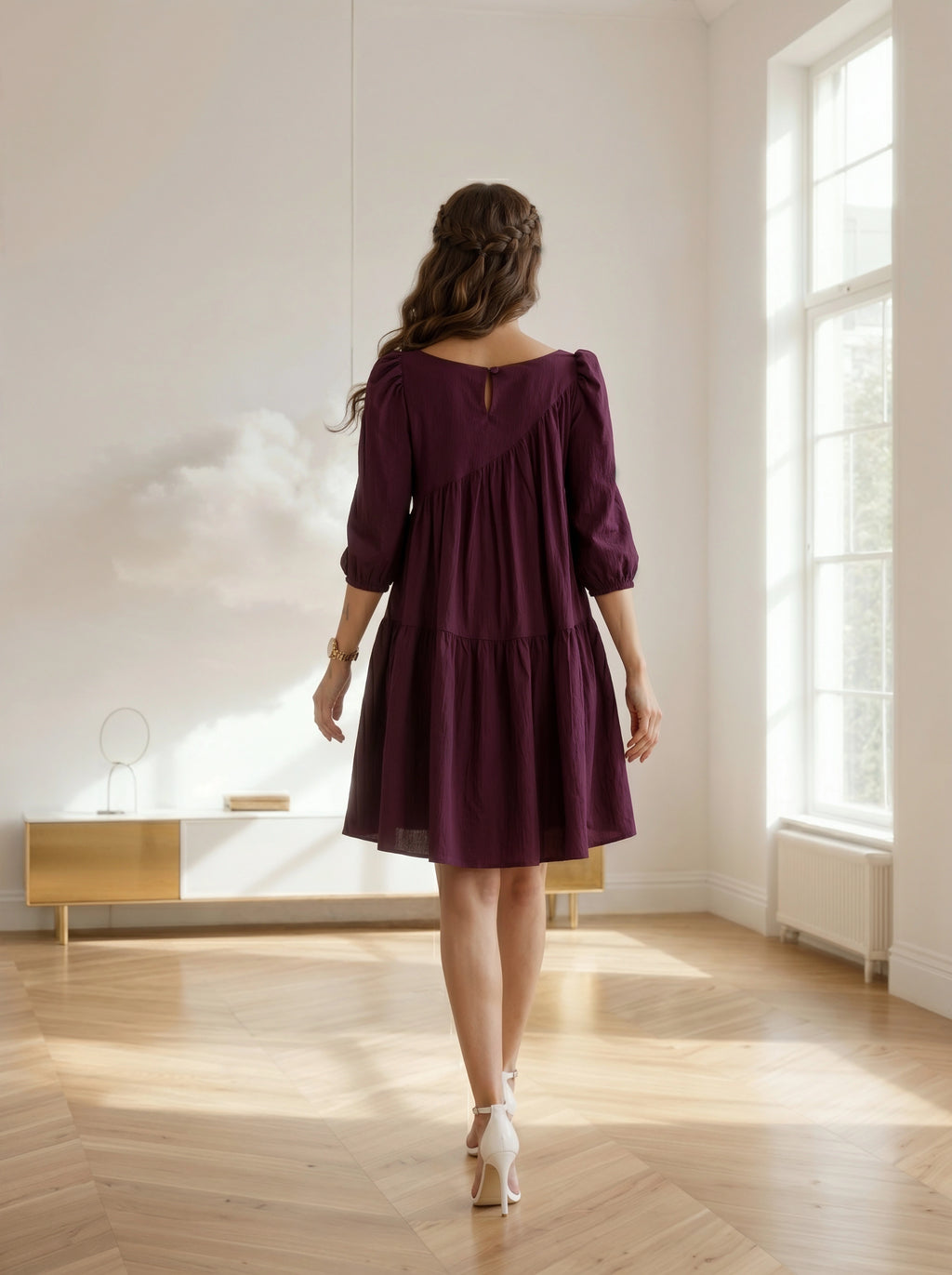 Woman in a purple dress standing in a bright room with large windows.