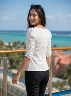 Woman in a white top and black pants standing on a balcony with ocean view