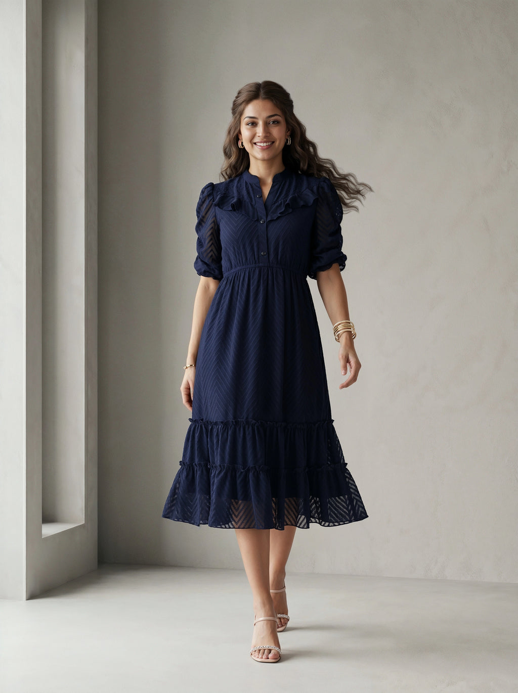Woman wearing a blue dress standing in front of a white wall with a window.